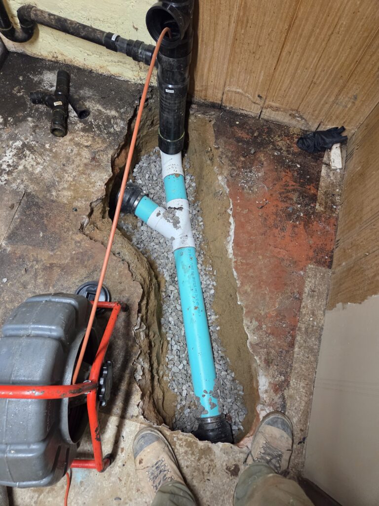 New drain piping laid in stone bedding below the opened concrete floor.