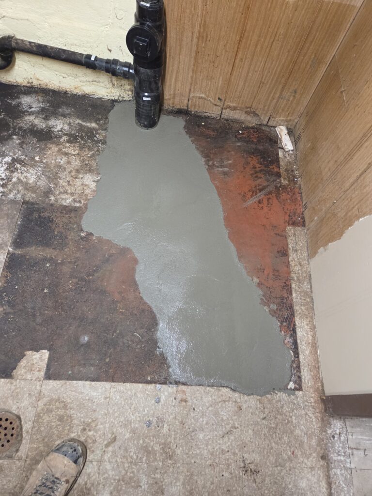 Kitchen drain stack with a capped cleanout above the restored concrete floor.